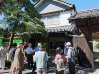 商家造りの建物の前に何人かの男女が集まって眺めている様子の写真