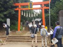 オレンジ色の鳥居の前に立っている人たちや、鳥居をくぐり抜けて歩いている人達のフィールドワークの様子の写真