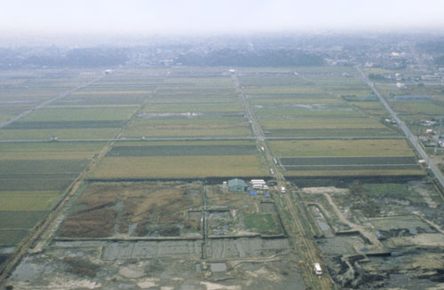 奥が霞がかっている一面田んぼのような風景を上空から撮った写真