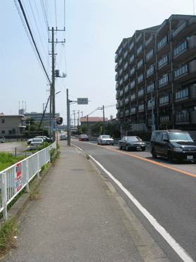 マンションの横の道路を車が数台走っており、道路の途中に「市原市」の看板がたっている写真
