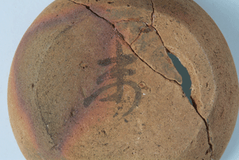 底に未(ひつじ)と書かれた、所々ひび割れて欠けている赤茶色の器の土器の写真