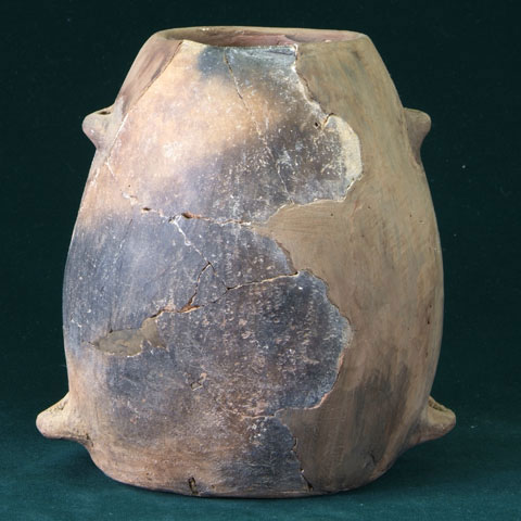 黒い背景に、下部と上部の左右合わせて4箇所にアーチ状の突起がある薄茶色の壺型土器の写真