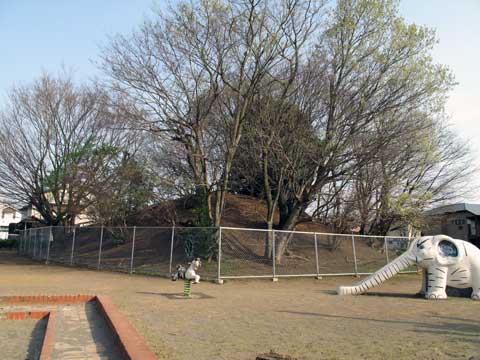 右手に白いぞうの滑り台がある公園の真ん中にフェンスで囲まれた丘がある写真