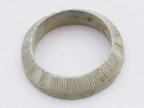 白い背景に、イモガイ製の腕輪をモデルにした石製品で作られた円形のデザインに縦に溝がついているブレスレットである石釧の写真