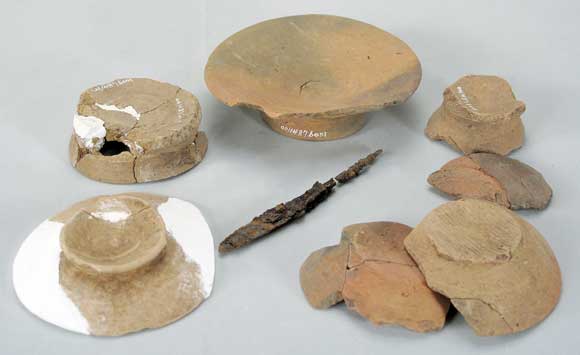 1487円形土抗で出土した遺物群で中央に鉄鏃、それを囲むように小型の土師器杯・足高高台土器など計8点が一緒に並べられている写真
