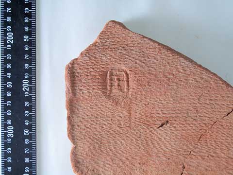 茶色の「周」と書かれた文字瓦の写真、横には大きさを示す定規がある