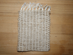 薄茶色の毛糸を左から右へ、そして反対に折り返しというのを繰り返し、縦にも毛糸を編んで上で結ばれてつくられた四角の布の写真