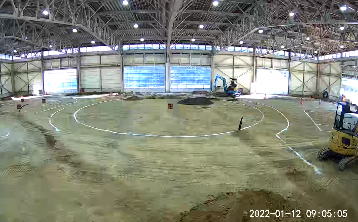重機などが入った広い館内の地面に円などの線が引かれている工事前の写真