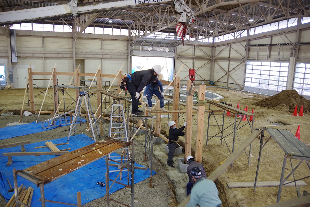 作業員達がクレーンを使って梁や柱を組み立てている写真