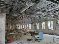 天井が剝き出しになっている室内に複数の脚立などが置かれている改修工事現場の写真