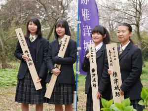 紫色の幟を挟んで女子高生が2名ずつ椎津城跡の標柱・案内板をそれぞれ持って並んで立っている写真