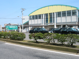 駐車場にタクシーが数台停車しており、丸いアーチ型の屋根で上部が薄黄色のJR八幡宿駅の外観写真