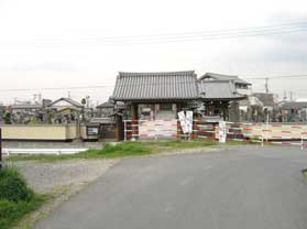 赤と白のフェンスの奥に妙経寺の山門が見えている写真