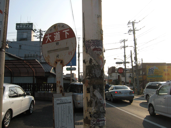 「大道下」と書かれたバス停と、片側一車線の道路の両側に建物が建っている写真