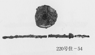 円の形の残っている紡輪、直接白で10桁の数字が書かれている、その下に二箇所折れのある紡軸、こちらも右端に直接白く数字のようなものが書いてある写真、写真右下には220号住-54と書かれている