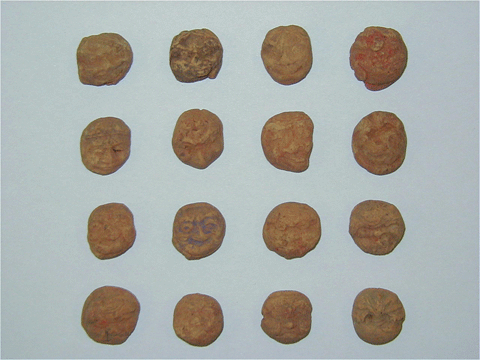 小さいクッキーのような丸い形で色々な人物の表情で作られた16個の泥めんこの写真