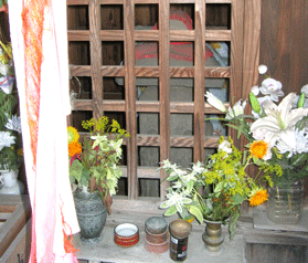 小祠の前に黄色や白色の花が供えられ、小祠の中には六地蔵石幢が祀られている写真
