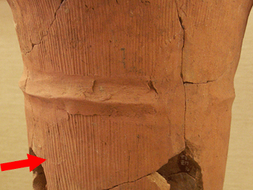 茶色の筒状の焼き物に何本もの縦に伸びた筋が入っている箇所を赤い矢印で示している写真