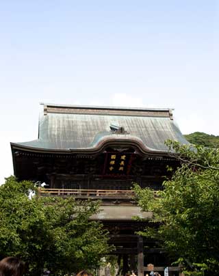 建物の両脇に樹木が植えられ、上層に「建長興国禅寺」の大扁額が掛けられている古い木造づくりの建長寺の山門の写真
