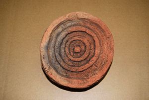 一部が黒ずんだ茶色い三重の紐状に表現されている丸の模様がある軒丸瓦の写真。