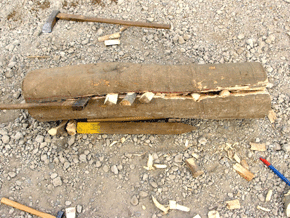 丸太が横たわり、半分のところで裂け目ができており、裂け目に小さな斧や木製のかけらがいくつか刺さっている様子の写真