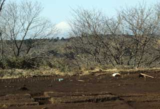 何も植えられていない畑の向こうにある一段高くなった段差の向こうから見える雪の降り積もった富士山の写真