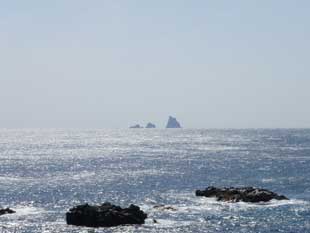 海の手前に見える岩場と、遠くには3つ島が並んでいるのが見える写真