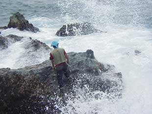 荒波の立つ岩場に男性が立っている写真