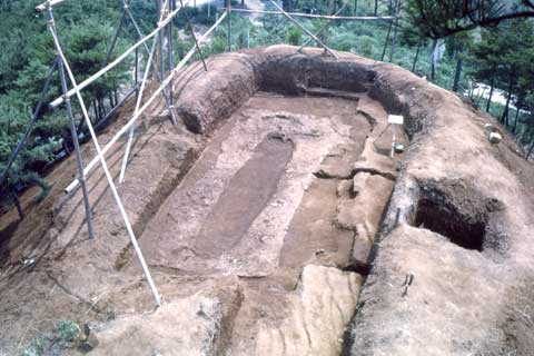 角が丸く掘られた左側に埋葬施設の跡が残っている大型前方後円墳を上から撮影した写真