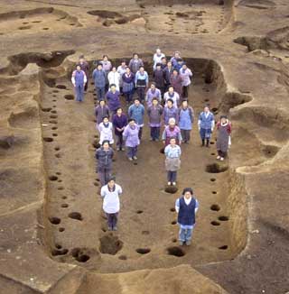 掘り下げられ、点々と穴が空いている地面に立つ複数の人々を上から写した写真