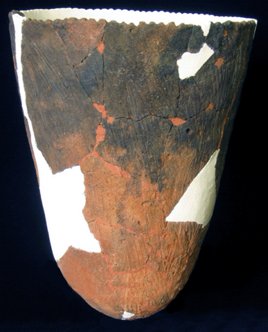 先の丸い円錐を逆にした形で赤土のような色をしており、上部が黒ずんでいる土器の写真