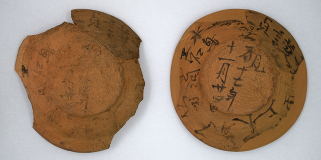墨汁で文字が書かれた茶色い器のような土器が2つ並んでいて、左側は割れ欠けがあり文字も薄く、右側は円形で器表面の形も書かれた文字もはっきりしている写真