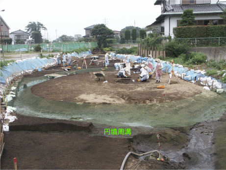 発掘が行われている円墳とその周溝の画像
