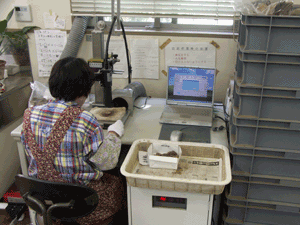 右側にノートパソコンを置いた机の上で機械の前に座った女性が作業している写真