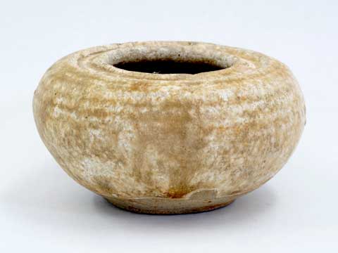 黄土色に白色がまだらに入っており、上部に横筋が入った碗のような形をした花瓶のような小さな壺の写真