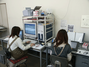 ブラウン管型のパソコンで作業をしている女性とその隣で書類を見ている女性の写真