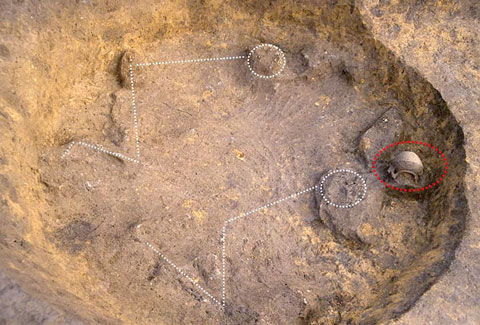 穴を掘られたところに発見された埋葬人骨と注口土器の出土状況の写真
