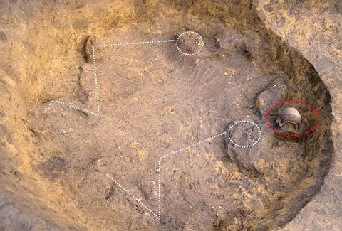 穴を掘られたところに発見された埋葬人骨と注口土器の出土状況の写真