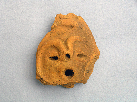 黄土色で顔をかたどっている土器の装飾の顔面把手の表側の写真