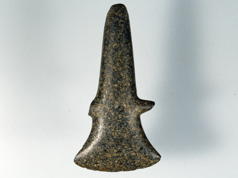表面が黒く、斧の刃を縦にしたような形で中央に突起がある石器の写真