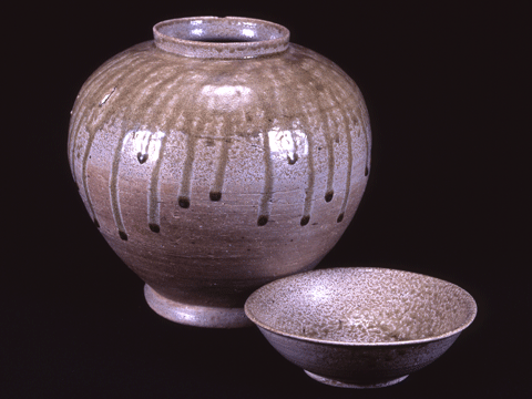 黒い背景に、薄茶色のまだらな色に茶色の液が垂れているような模様の壺と、壺と同じ色をした椀の写真