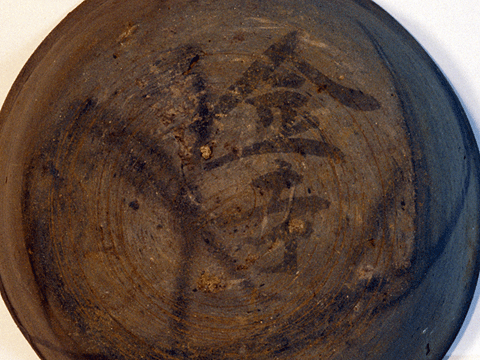 白い背景に、金寺と文字が書かれている、まだらな茶色い丸形の土器の写真