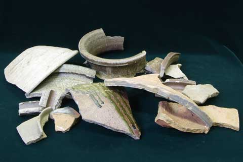 深緑色の敷物の上に白や薄オレンジ色の陶器の破片が重なり置かれている写真